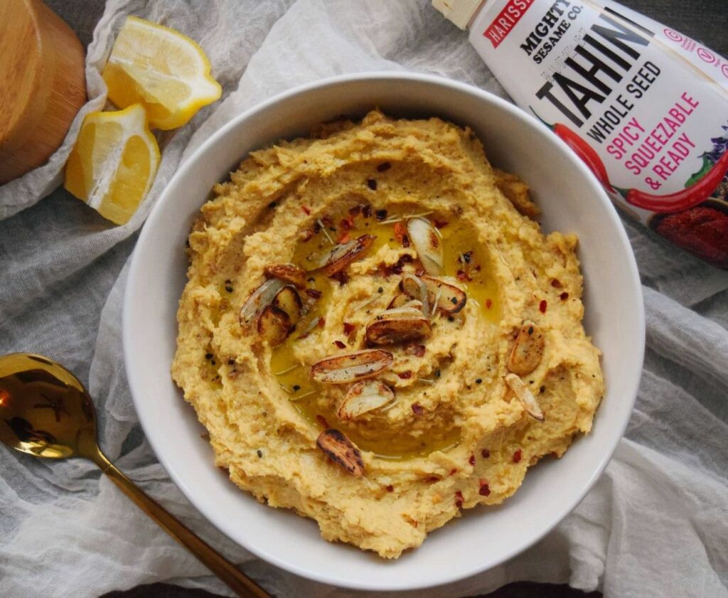 Spicy tahini hummus in a bowl with lemon and grilled garlic, featuring Mighty Sesame Tahini.