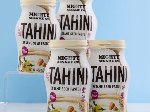 Four tubs of Mighty Sesame Tahini arranged on a light blue background.