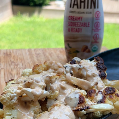 Roasted cauliflower florets drizzled with tahini sauce, garnished with herbs and spices, served in a skillet.