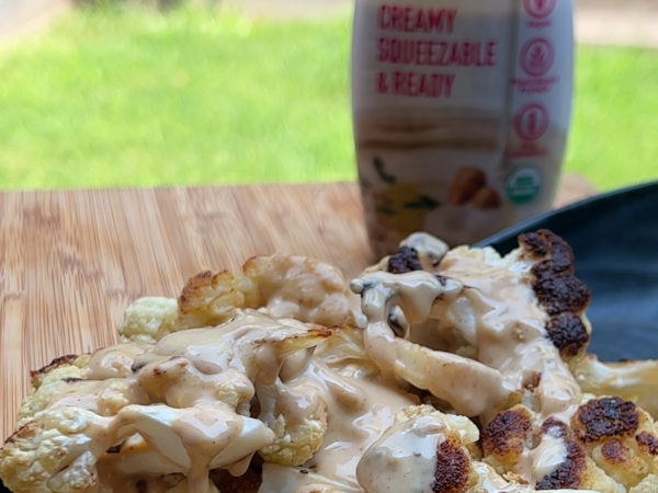 Roasted cauliflower florets drizzled with tahini sauce, garnished with herbs and spices, served in a skillet.