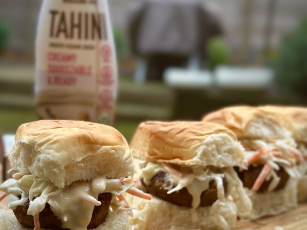Three falafel sliders topped with fresh veggies and drizzled with tahini, served on mini buns.
