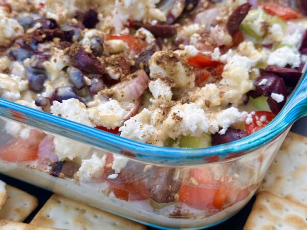 glass dish with 7 layer dip, made from mighty sesame tahini hummus and served with crackers on the side