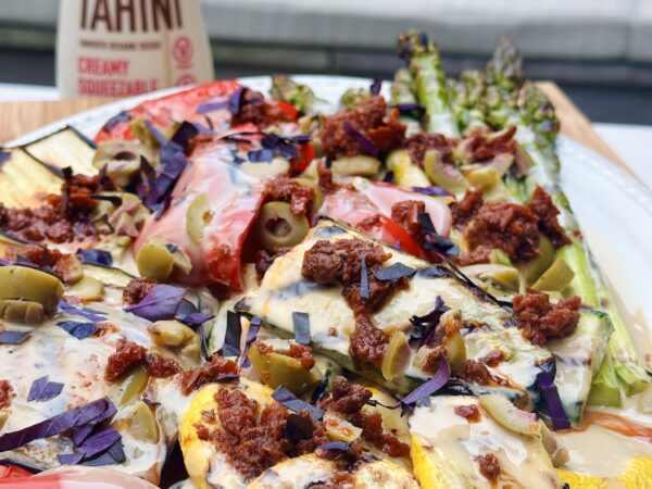 Colorful grilled vegetables, including bell peppers, zucchini & asparagus, drizzled with tahini sauce and topped with herbs.