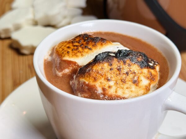 Cup of rich hot cocoa topped with toasted marshmallows and a drizzle of tahini, creating a nutty twist on a cozy beverage.