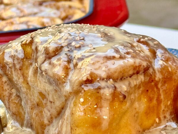 Soft, golden-brown cinnamon roll drizzled with a creamy tahini glaze, offering a unique twist on a classic dessert.
