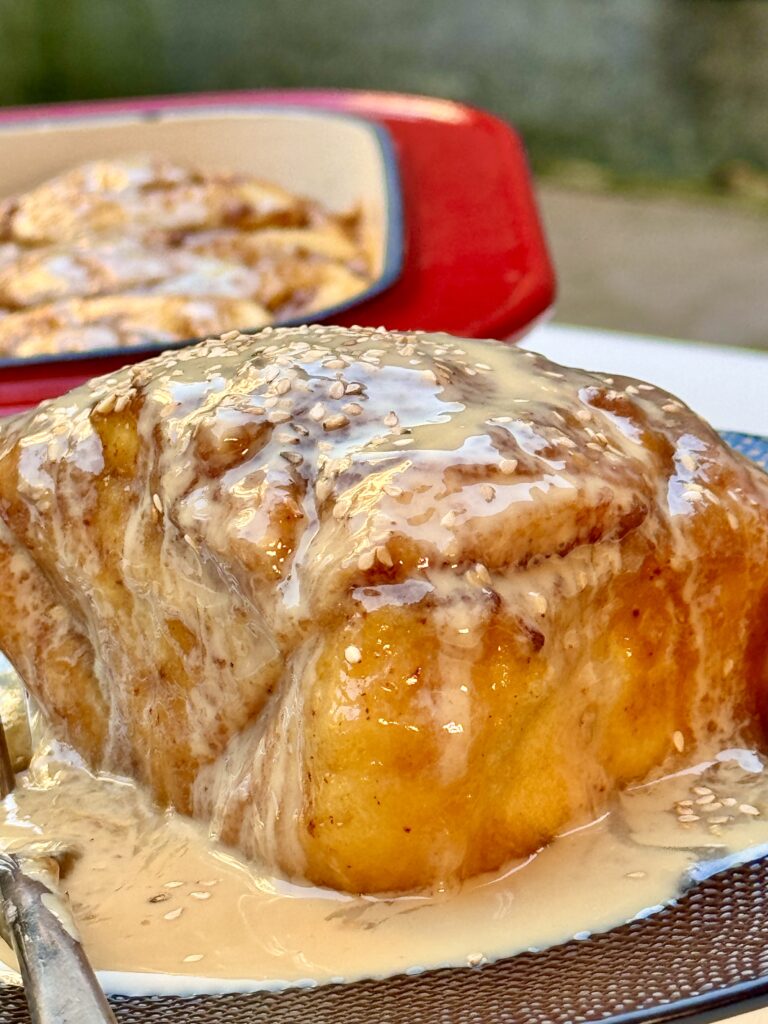 Soft, golden-brown cinnamon roll drizzled with a creamy tahini glaze, offering a unique twist on a classic dessert.
