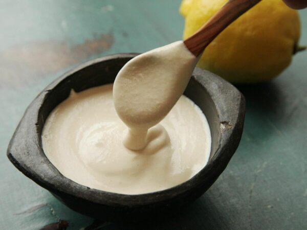 Spoon lifting thick tahini from a small black bowl; lemon in the background.