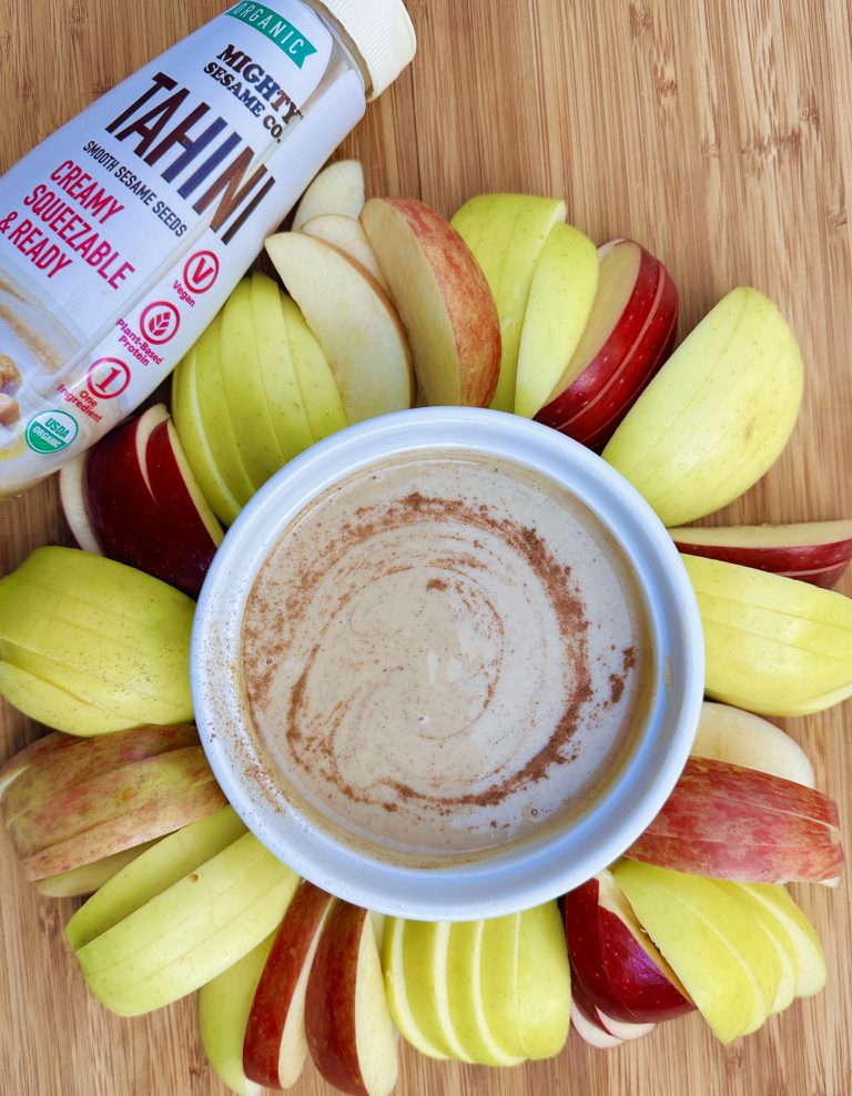 Bowl of creamy apple tahini dip made with Mighty Sesame Tahini, surrounded by fresh apple slices.