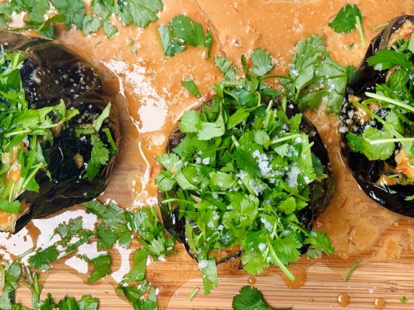 Roasted eggplant halves topped with fresh herbs like parsley and cilantro, drizzled with creamy tahini sauce.