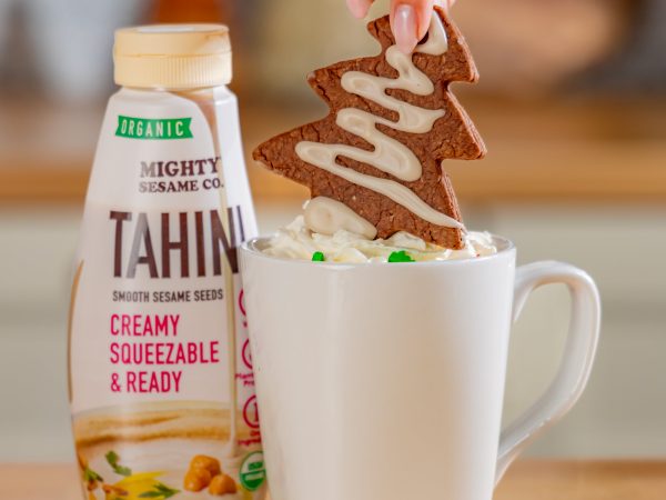 Bottle of Mighty Sesame Tahini next to a mug being drizzled with tahini.