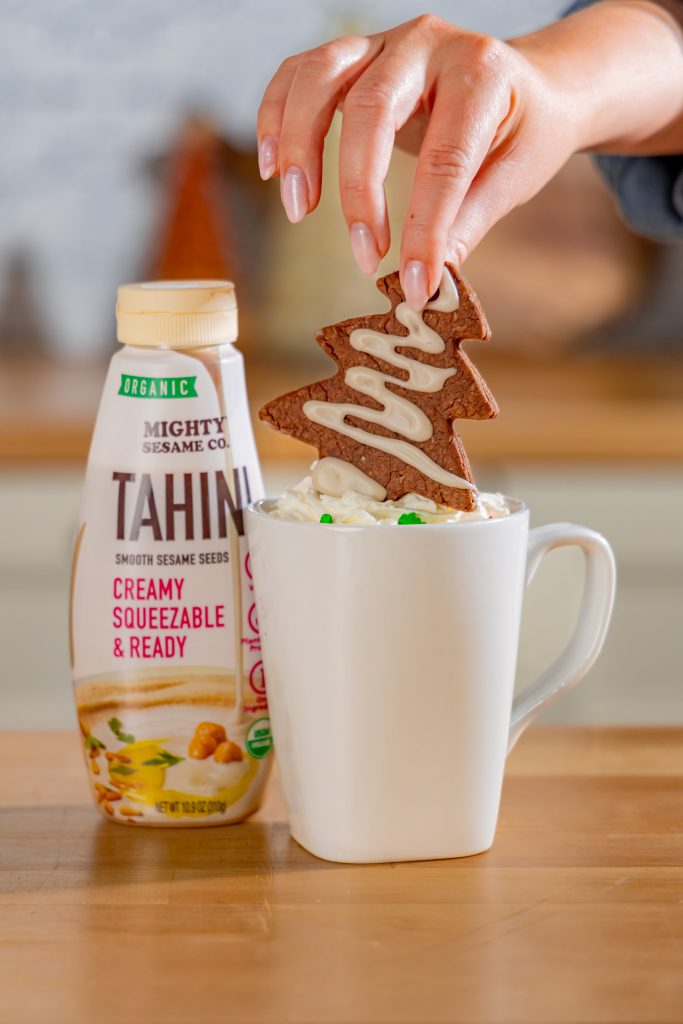 Bottle of Mighty Sesame Tahini next to a mug being drizzled with tahini.