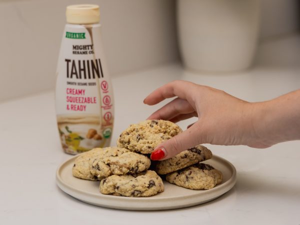 A bottle of Mighty Sesame Tahini cream is placed next to a plate of freshly baked cookies.