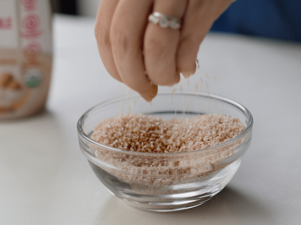 Hand dropping sesame seeds into a bowl of sesame seeds.