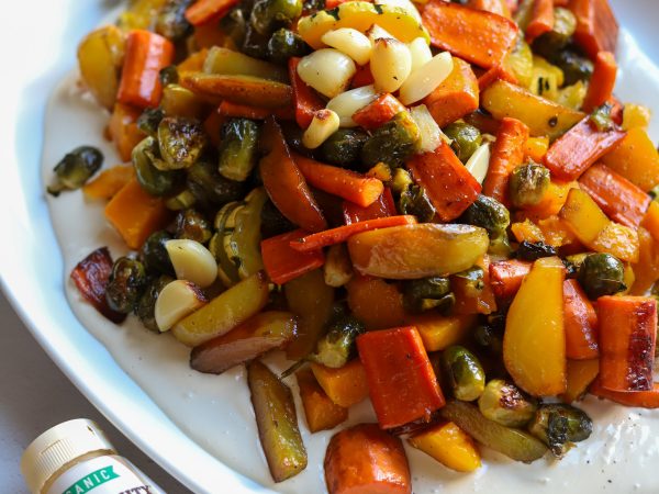 A plate of colorful roasted vegetables with bell peppers, carrots, and onions, paired with Mighty Sesame Tahini.