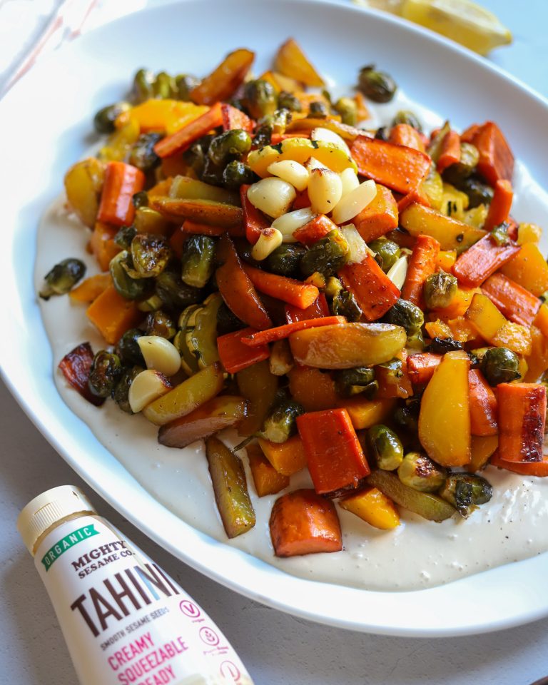 A plate of colorful roasted vegetables with bell peppers, carrots, and onions, paired with Mighty Sesame Tahini.
