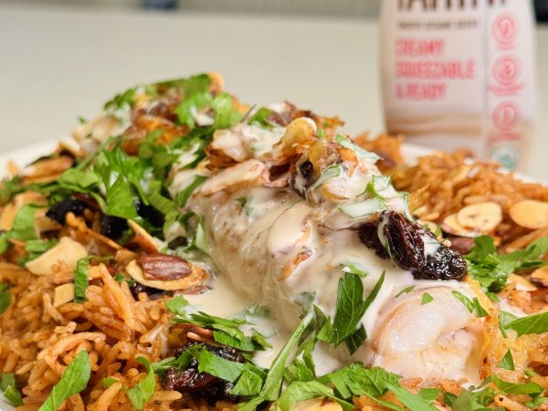 Colorful salad topped with chicken, herbs, and sesame sauce, accompanied by a can of Mighty Sesame tahini.