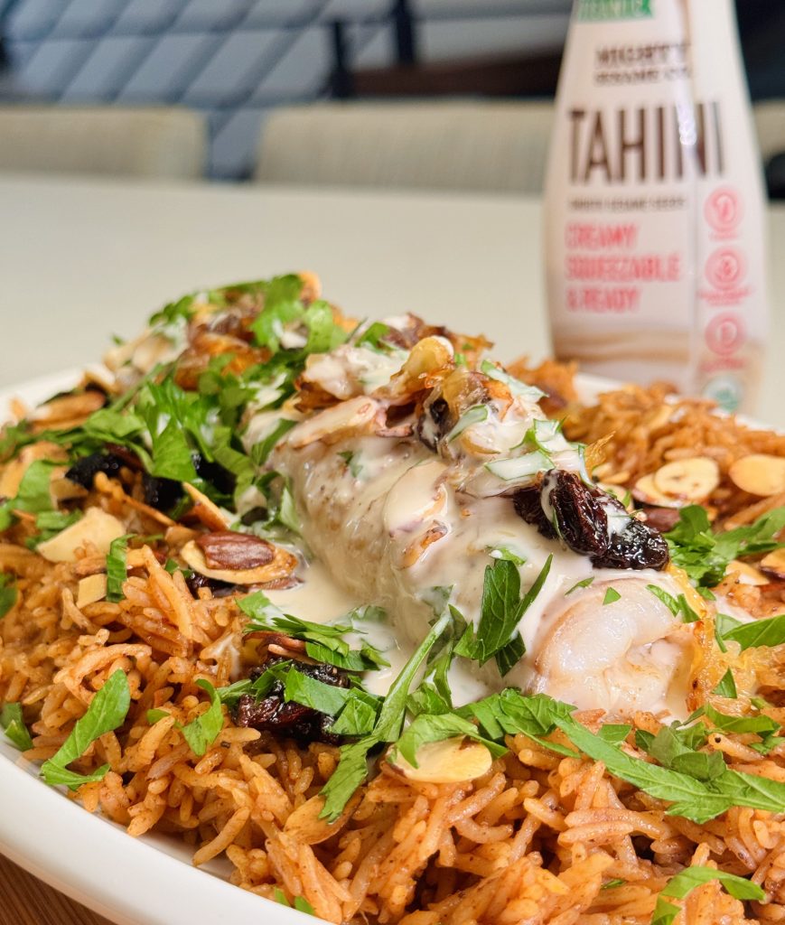 Colorful salad topped with chicken, herbs, and sesame sauce, accompanied by a can of Mighty Sesame tahini.