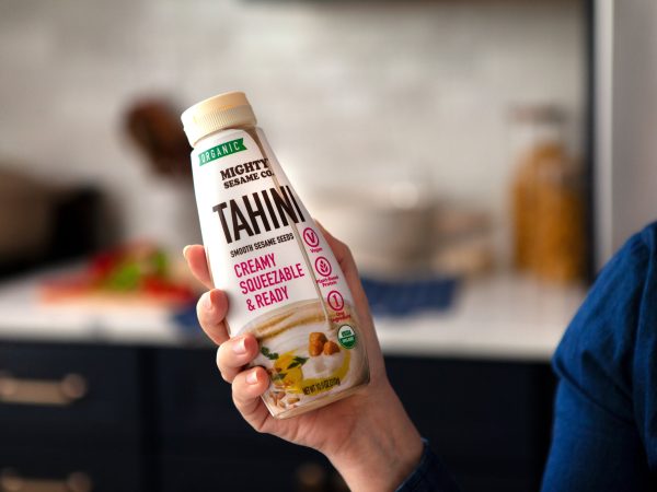 Mighty Sesame Tahini squeeze bottle held in hand, ready to use.