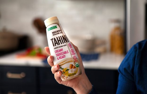 Mighty Sesame Tahini squeeze bottle held in hand, ready to use.