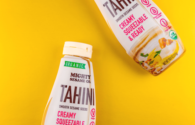 Two Mighty Sesame Co. tahini bottles on a yellow background, showcasing organic, vegan, and creamy, squeezable features.