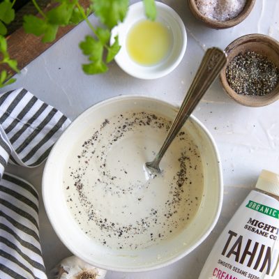 Tahini dressing ingredients: tahini, lemon, garlic, oil, salt, and pepper. Bowl with dressing and spoon.