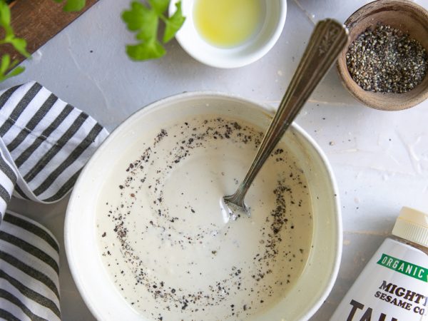 Tahini dressing ingredients: tahini, lemon, garlic, oil, salt, and pepper. Bowl with dressing and spoon.