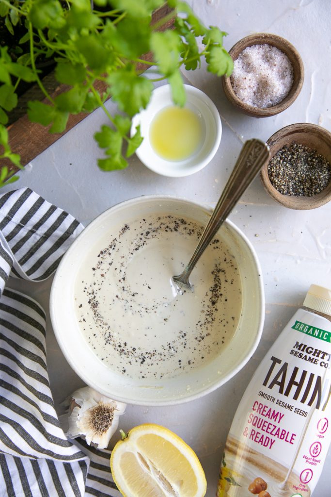Tahini dressing ingredients: tahini, lemon, garlic, oil, salt, and pepper. Bowl with dressing and spoon.
