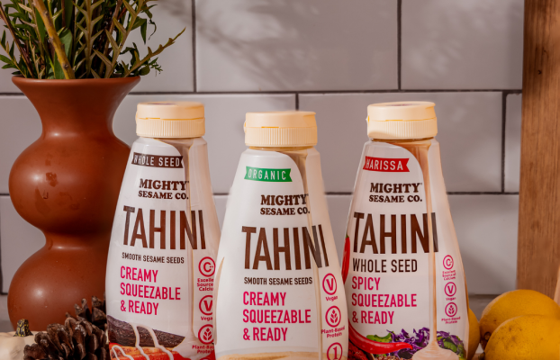 Three Mighty Sesame Co. Tahini squeeze bottles—Whole Seed, Organic, and Harissa Spicy—are displayed on a kitchen setup.