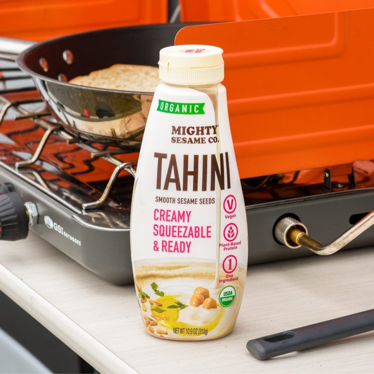 Mighty Sesame Co. Tahini bottle on a camping stove. Vegan, creamy tahini ready to use.
