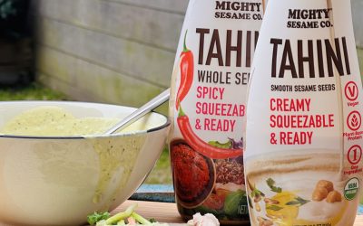 Two tahini squeeze bottles beside a bowl of green sauce and wrap fixings.