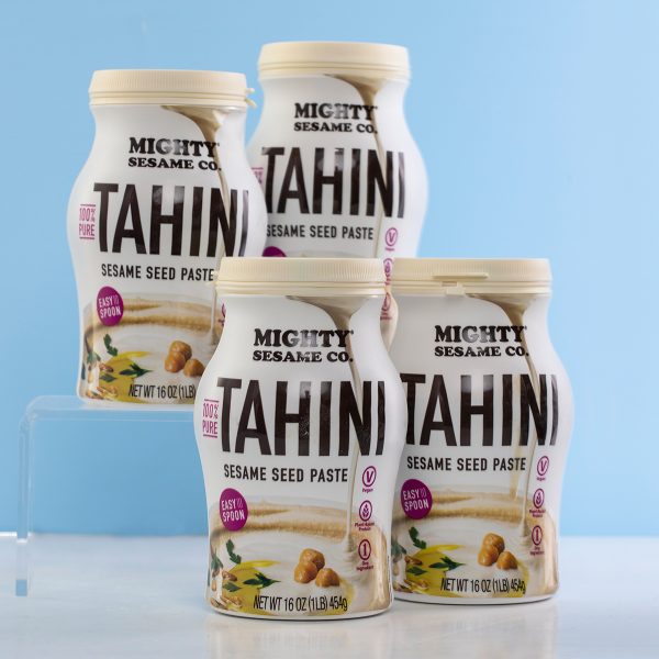 Four tubs of Mighty Sesame Tahini arranged on a light blue background.