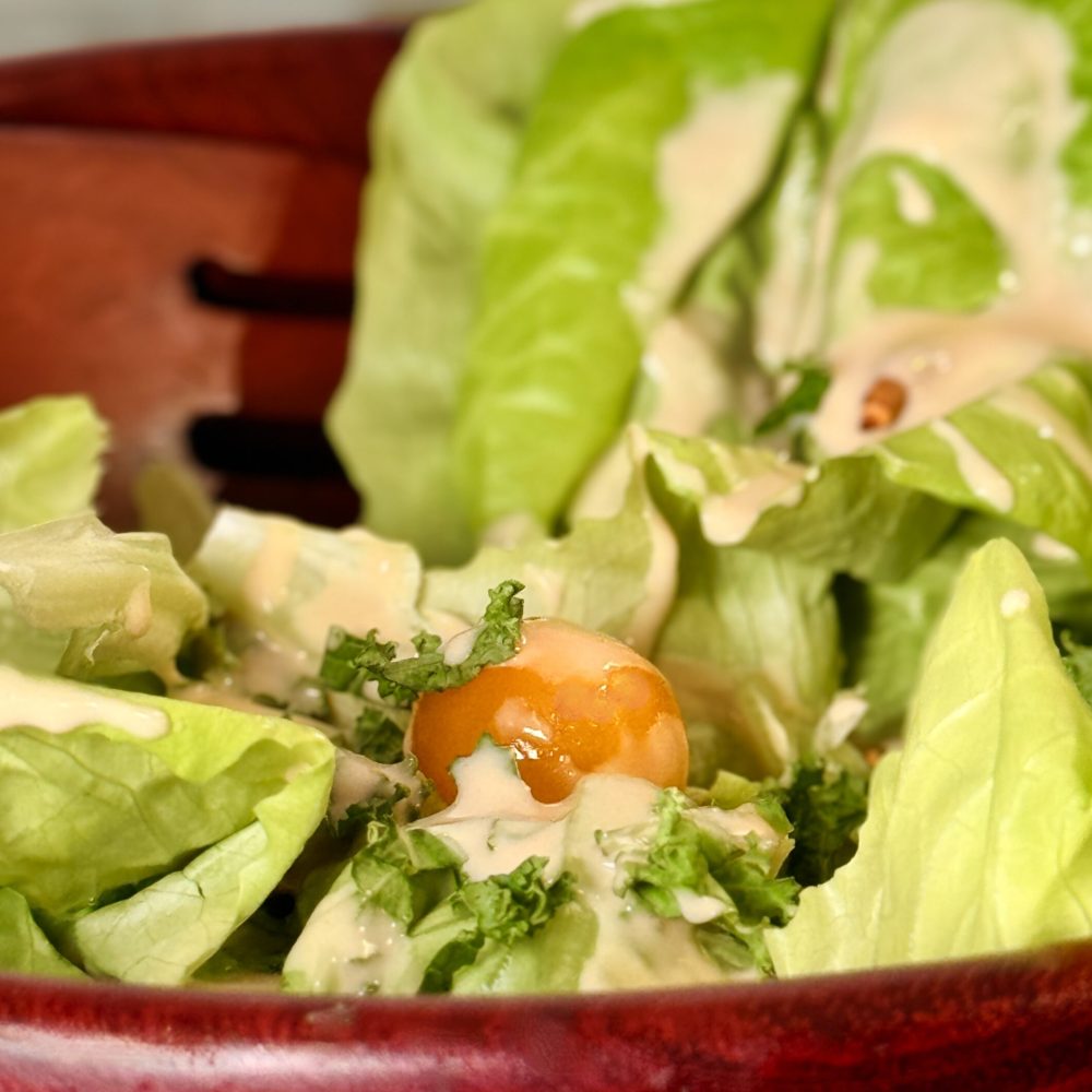 Fresh green salad with avocado, cherry tomatoes, and cucumber, drizzled with a tangy miho tahini dressing.