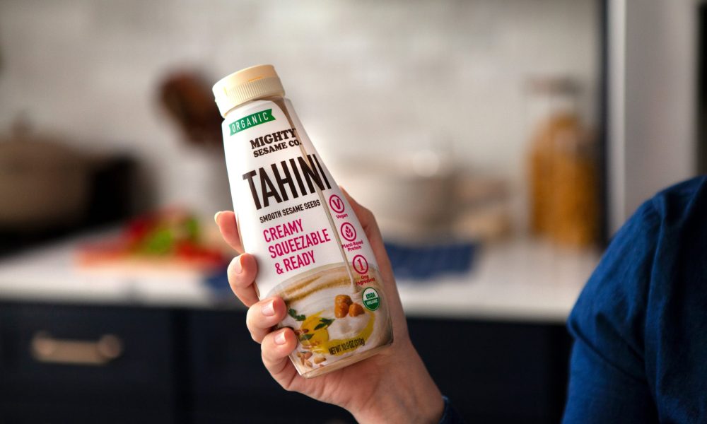 Mighty Sesame Tahini squeeze bottle held in hand, ready to use.