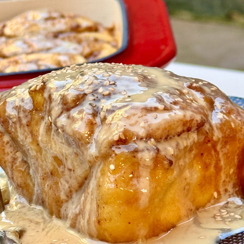 Soft, golden-brown cinnamon roll drizzled with a creamy tahini glaze, offering a unique twist on a classic dessert.