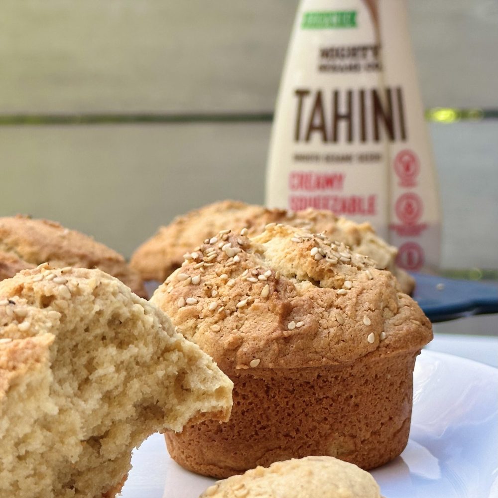 Sesame-topped tahini muffins with a Mighty Sesame tahini bottle in the background.